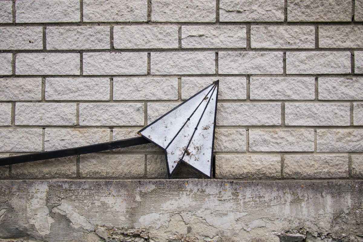 A paper plane, representing sending email, against a light, grey, brick wall